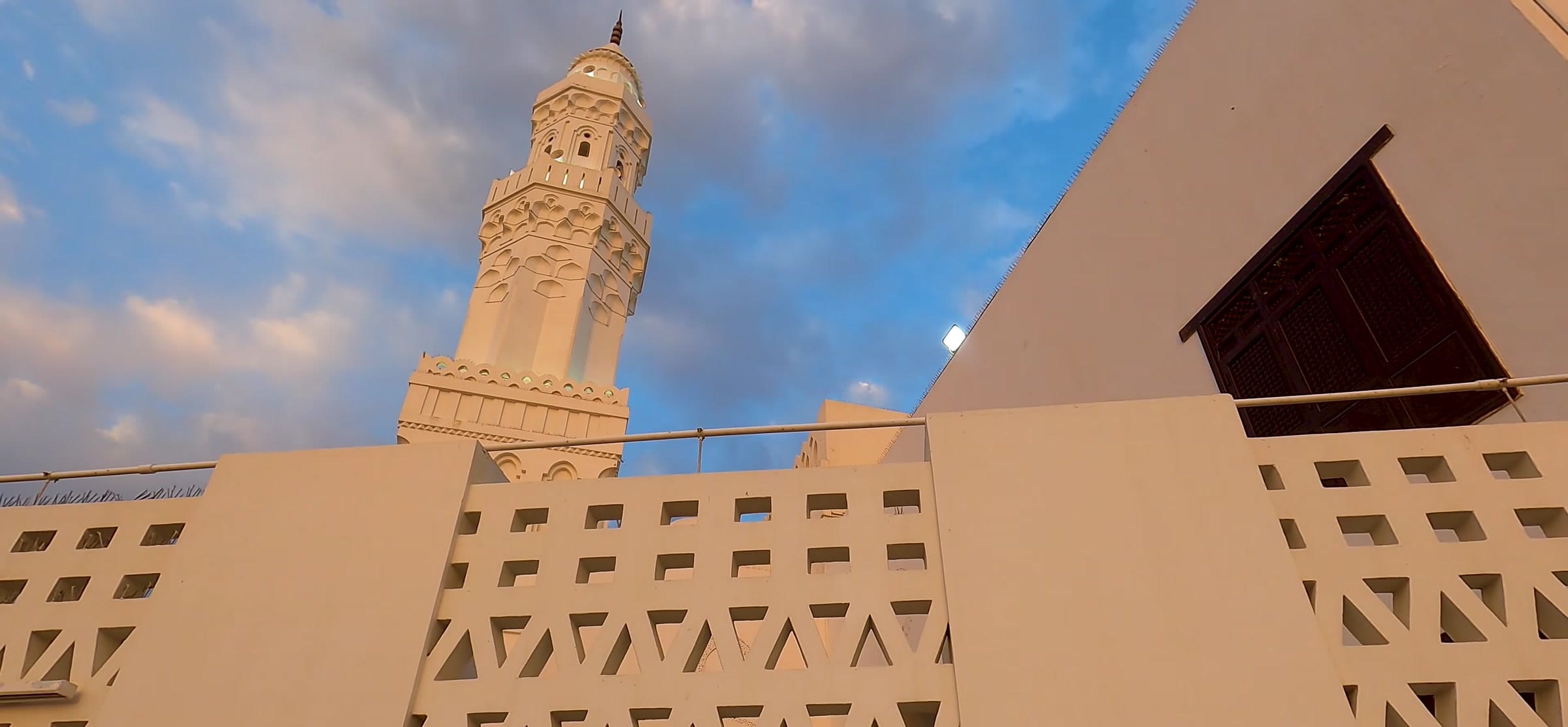 Geometric latticework and a minaret against open sky.
